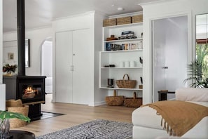 Una sala de estar con chimenea, estanterías blancas con cestas y libros, un sofá blanco y una alfombra estampada.