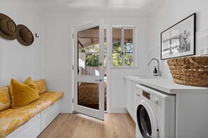 Een wasserette met een wasmachine, een wasbak en een mand op het aanrecht.