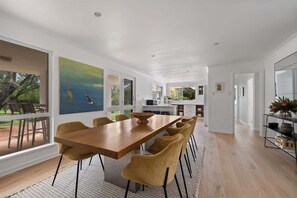 A modern dining area with a wooden table and matching chairs, a large painting on the wall, and a view of the outdoors.