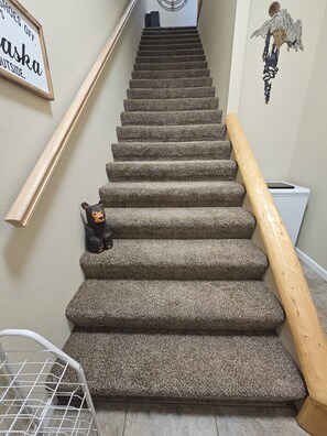 A carpeted staircase with a wooden handrail, a bear figurine, and a wall sign.