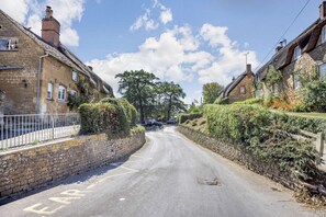 Drive through a charming rural landscape along a narrow road lined with traditional stone houses.