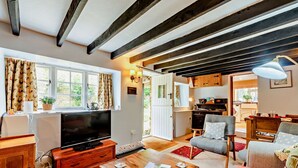 Una sala de estar acogedora con televisor, muebles de madera y una cocina al fondo.