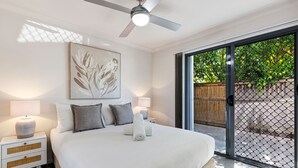 A bedroom with a large bed, two bedside tables with lamps, a ceiling fan, and a sliding glass door to the outside. - MARJ12- Stylish and Spacious Apartment  (Mooloolaba)