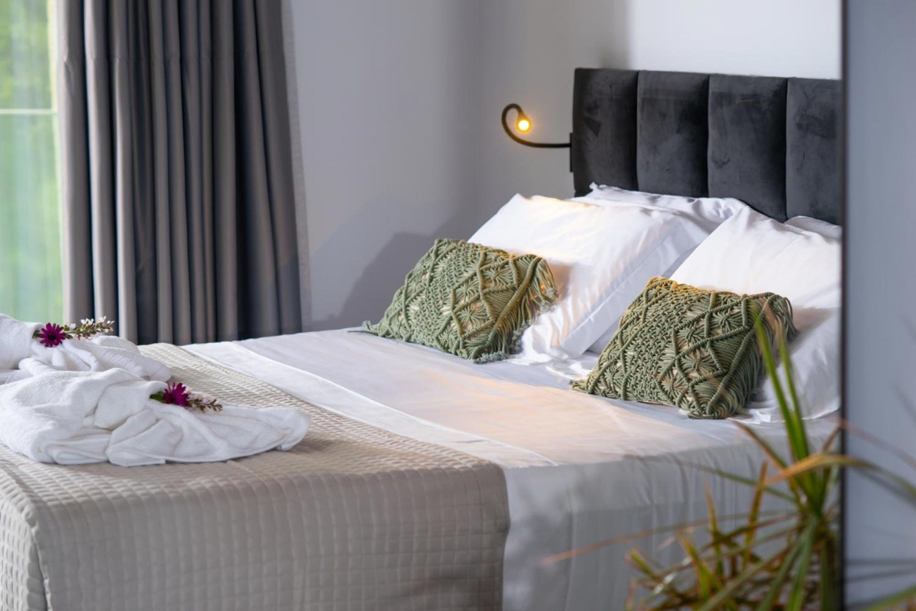 A neatly made bed with white linens, two green patterned pillows, and a dark headboard.