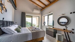 A bedroom with a bed, bedside table, vanity, and a window with a view. - Prenari Villa in Paxi (Paxos)