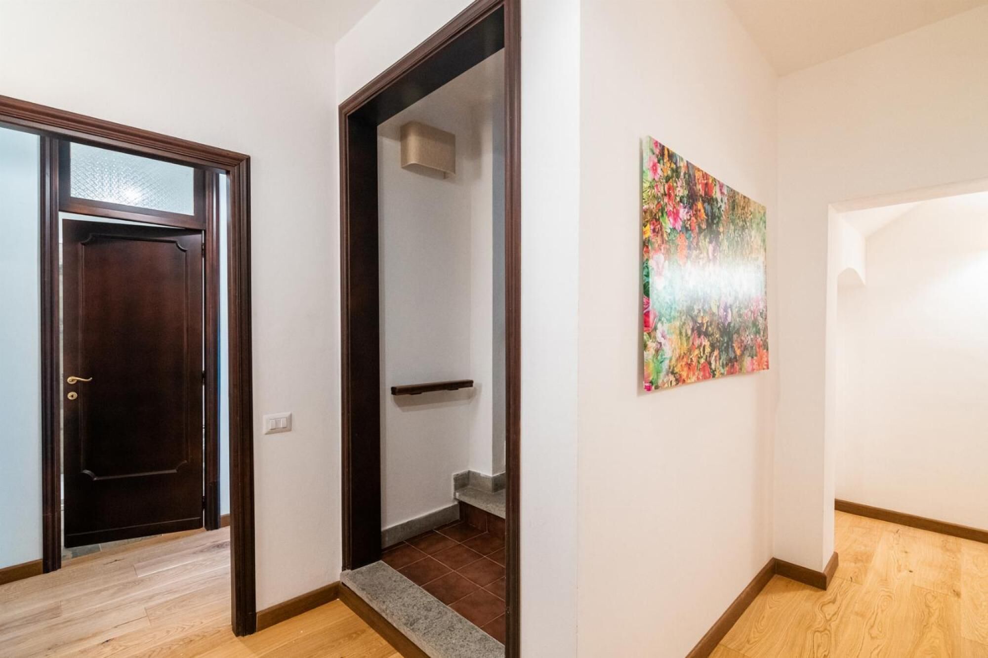 A hallway with a wooden door, a staircase, and a colorful abstract painting on the wall.