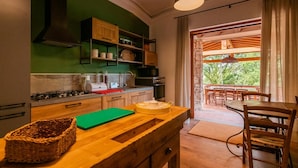Uma cozinha com armários de madeira, bancada verde e vista para um pátio externo com mesa e cadeiras.
