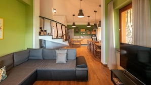 Uma sala de estar com sofá, televisão e escada que dá para uma cozinha.