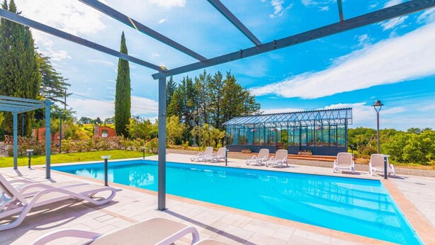Piscina com espreguiçadeiras e área coberta com estrutura de vidro.