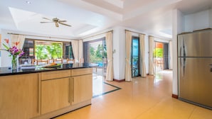 A modern kitchen with a central island, a large refrigerator, and sliding glass doors leading to a balcony with a view of greenery.