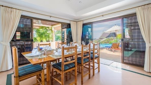 A dining area with a table set for four, wooden chairs with blue cushions, and a view of a pool and greenery outside.