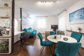 A modern living room with teal chairs, a white dining table, and a TV on a stand. - Top Location Beach & Downtown Split Apartment Park (Split)