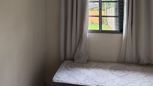 A room with a bed, an air conditioner, a window with curtains, and a view of the outside.