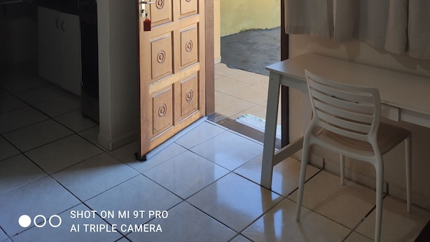 A room with a wooden door, a white chair, and a view of a yellow wall outside.
