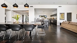 A modern kitchen with dark flooring, a dining area with a long table and chairs, and a living area with a sofa.