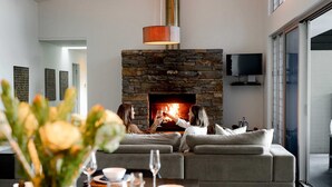 A modern living room with a stone fireplace, a sofa, and a dining area with a table set for two.