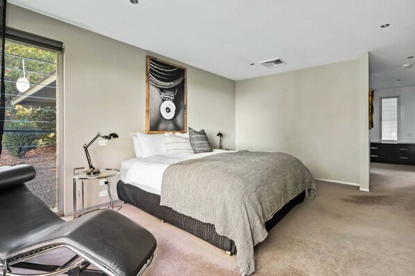A bedroom with a large bed, a desk with a chair, a window with blinds, and a painting on the wall.