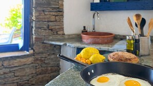 Eine Küche mit Steinwand, einem roten Topf, einer Bratpfanne mit Eiern und einem Holzlöffel.