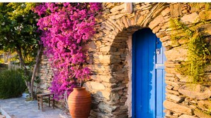 Ein Gebäude aus Stein mit einer blauen Tür, einem großen Terrakottatopf und rosa Bougainvillea-Blüten.