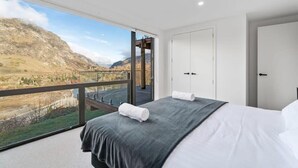 Ein Schlafzimmer mit großem Fenster, einem Bett, einem Kleiderschrank und Blick auf eine Berglandschaft.