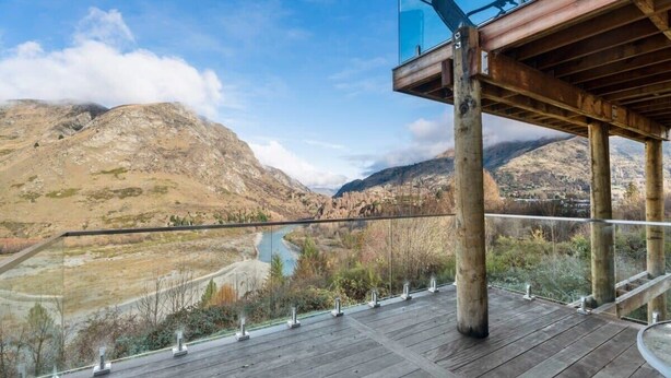 Eine Holzterrasse mit Glasgeländer mit Blick auf eine gebirgige Landschaft.