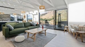 Ein großzügiger Wohnbereich mit einem grünen Sofa, einem Holztisch und einer großen Schiebeglastür, die auf einen Balkon mit Blick auf die Berge führt.