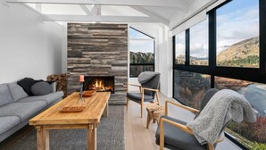 Ein modernes Wohnzimmer mit Kamin, einer Couch, einem Couchtisch und großen Fenstern mit Blick auf die Berge.