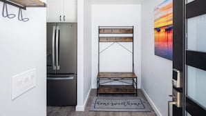 Une cuisine moderne avec un réfrigérateur en acier inoxydable, un banc en bois et un paillasson sur lequel est écrit « chez soi, quel bonheur ».