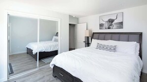 Une chambre avec un grand placard à portes coulissantes, un lit avec une literie blanche, une table de chevet avec une lampe et un tableau encadré au mur.