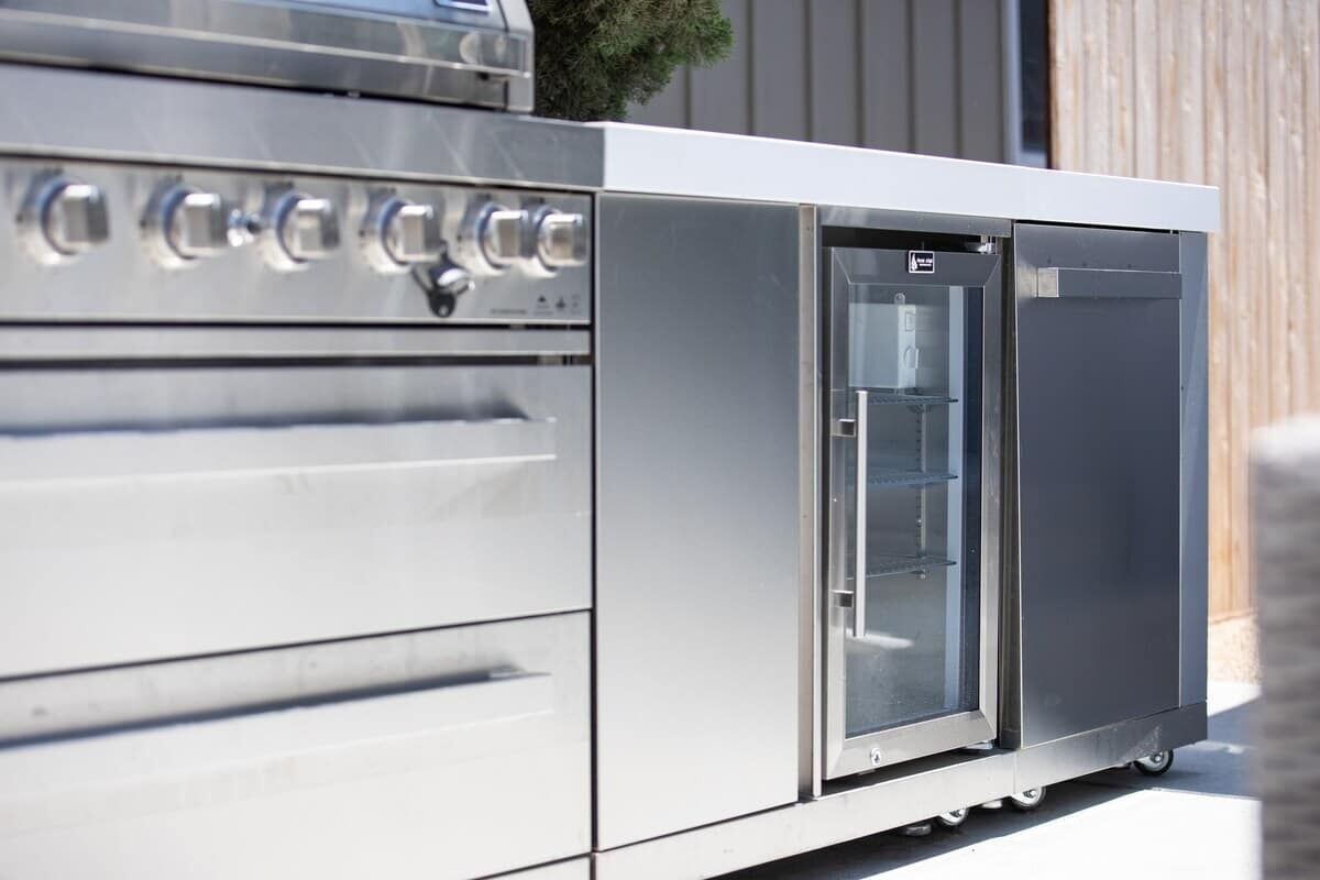 Eine Outdoor-Küche aus Edelstahl mit integriertem Kühlschrank und Backofen, ausgestattet mit mehreren Bedienknöpfen und einer Glastür.