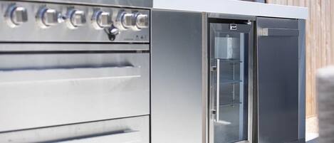 Eine Outdoor-Küche aus Edelstahl mit integriertem Kühlschrank und Backofen, ausgestattet mit mehreren Bedienknöpfen und einer Glastür.