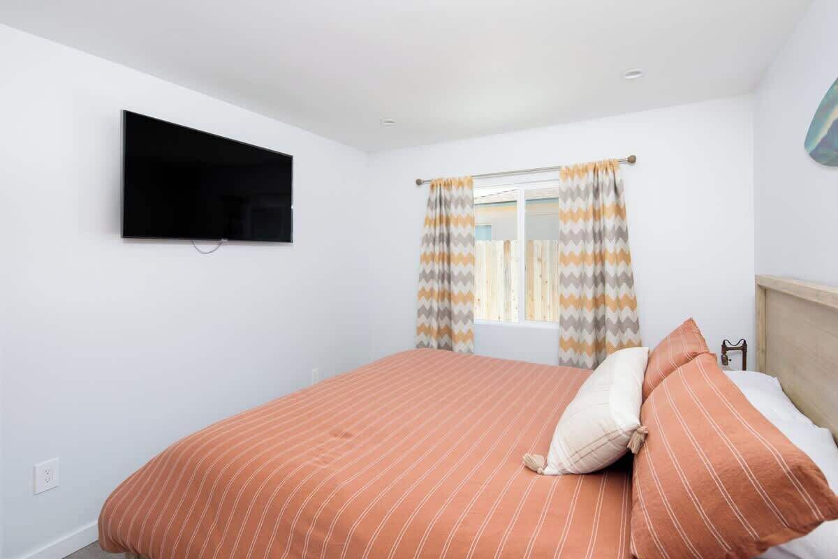 Une chambre à coucher avec un lit, un téléviseur fixé au mur et une fenêtre avec des rideaux.