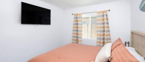 Une chambre à coucher avec un lit, un téléviseur fixé au mur et une fenêtre avec des rideaux.