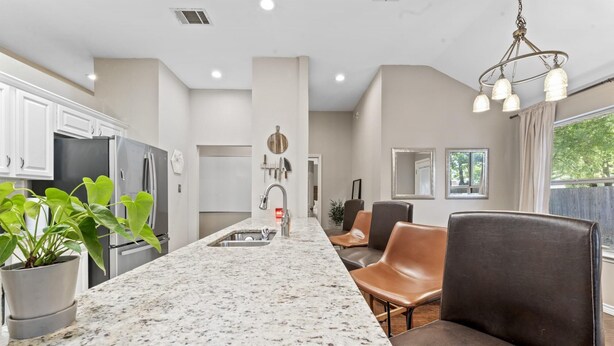 A modern kitchen with granite countertops, stainless steel appliances, and a central island. There are leather chairs and a dining area with a view of the outdoors. - Close to Kalahari King Beds Fast Wifi 3BR (Round Rock)