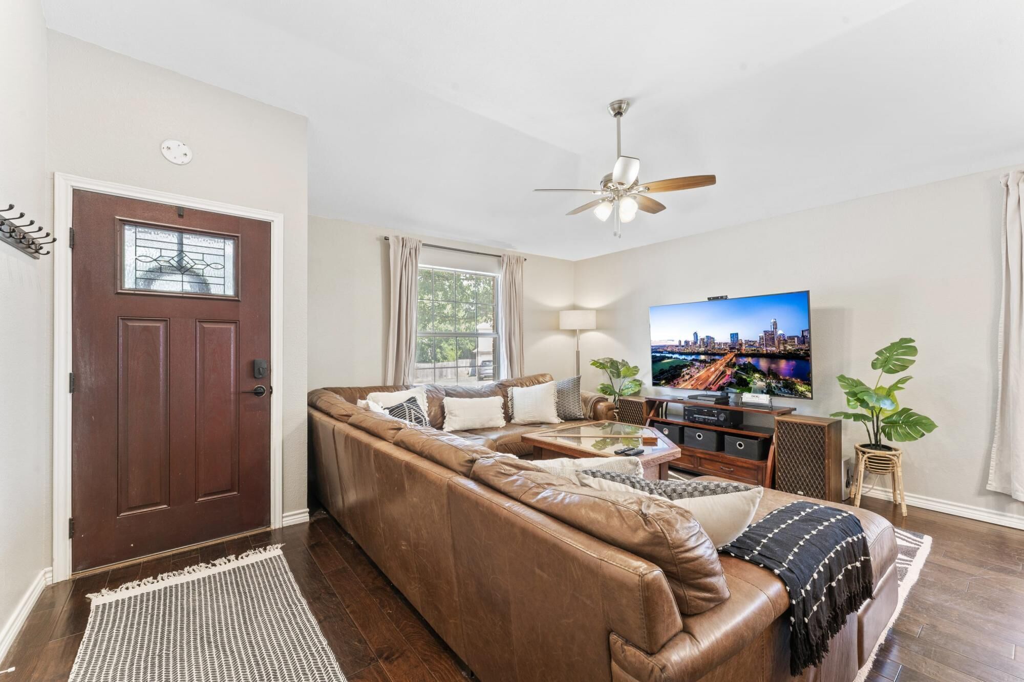 A living room with a brown leather sofa, a glass coffee table, a TV, and a ceiling fan.