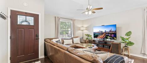 A living room with a brown leather sofa, a glass coffee table, a TV, and a ceiling fan.