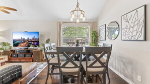 A dining area with a table and chairs, a television displaying a cityscape, and artwork on the walls. - Close to Kalahari King Beds Fast Wifi 3BR (Round Rock)