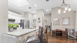 A modern kitchen with a central island, stainless steel appliances, and a dining area with wooden chairs and a glass cabinet. - Close to Kalahari King Beds Fast Wifi 3BR (Round Rock)