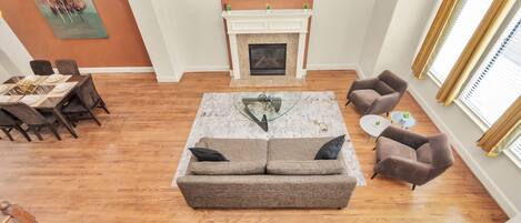A living room with a fireplace, a sofa, a dining table set, and a TV mounted on the wall.