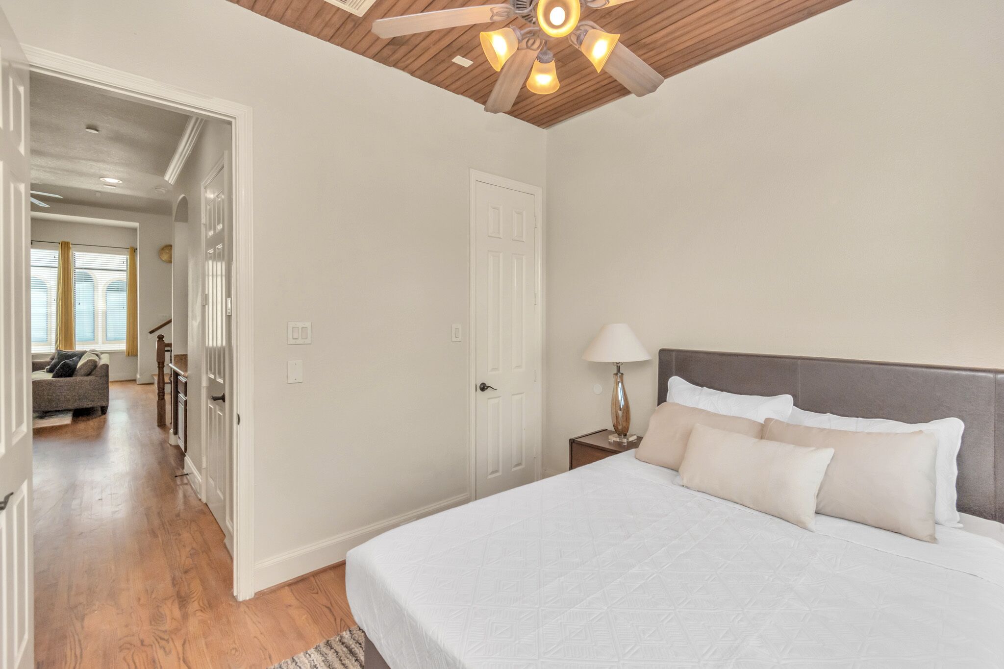 A bedroom with a bed, a nightstand, a lamp, a ceiling fan, and a door leading to another room.