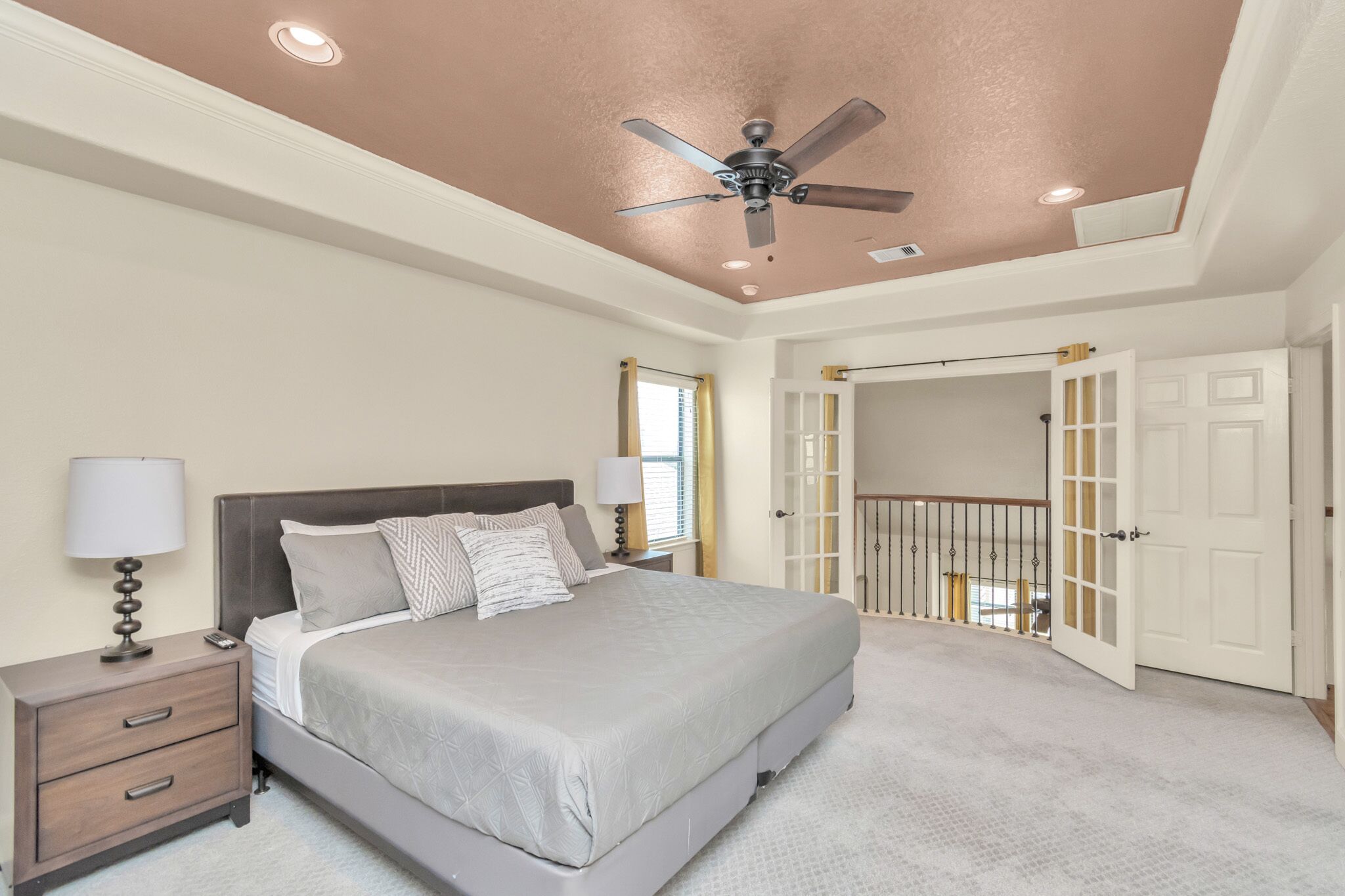 A bedroom with a bed, nightstands, a ceiling fan, and a door leading to a balcony.