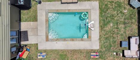 A rectangular swimming pool with a surrounding deck, a lounge chair, and a small table.