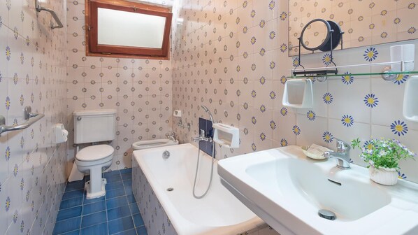 A bathroom with a toilet, bathtub, and sink, featuring a floral tile pattern on the walls and blue-tiled floor. - Retiro Perpignan in Alghero (Alghero)