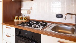 A kitchen with a gas stove, a sink, and a dishwasher. There are three decorative jars on the counter. - Casa Su Lizu in Tanaunella (Budoni)