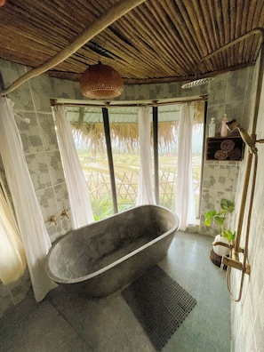 A bathroom with a freestanding bathtub, stone walls, a woven ceiling, and a view of a garden. - Pù Luông Ecocharm (Pu Luong)