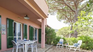 An outdoor patio with a table and chairs, a pergola, and a large tree providing shade. - Gli Oleandri di Procchio (Procchio)