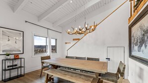 Uma ampla área de refeições com uma grande mesa de madeira, bancos e um lustre moderno.