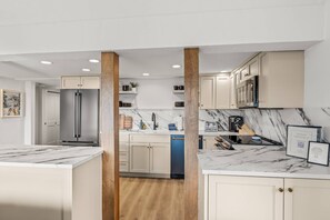 A modern kitchen with marble countertops, stainless steel appliances, and light wood flooring.