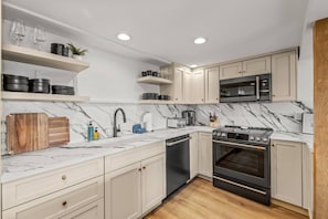 A modern kitchen with white cabinets, a black oven, a microwave, and a marble countertop. - Ski In/Walk Out, Hot Tub, Epic Views, W/D, & Games (Steamboat Springs)