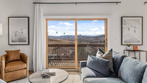 Sala de estar com uma grande porta de vidro deslizante que dá para uma varanda com vista para as montanhas.